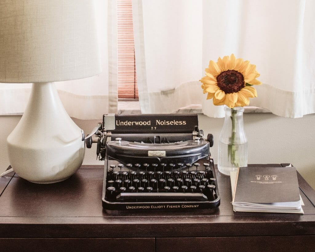 typewriter on a desk next to a sunflower in a vase
