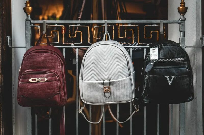 Expensive backpack style handbags hanging on a metal gate