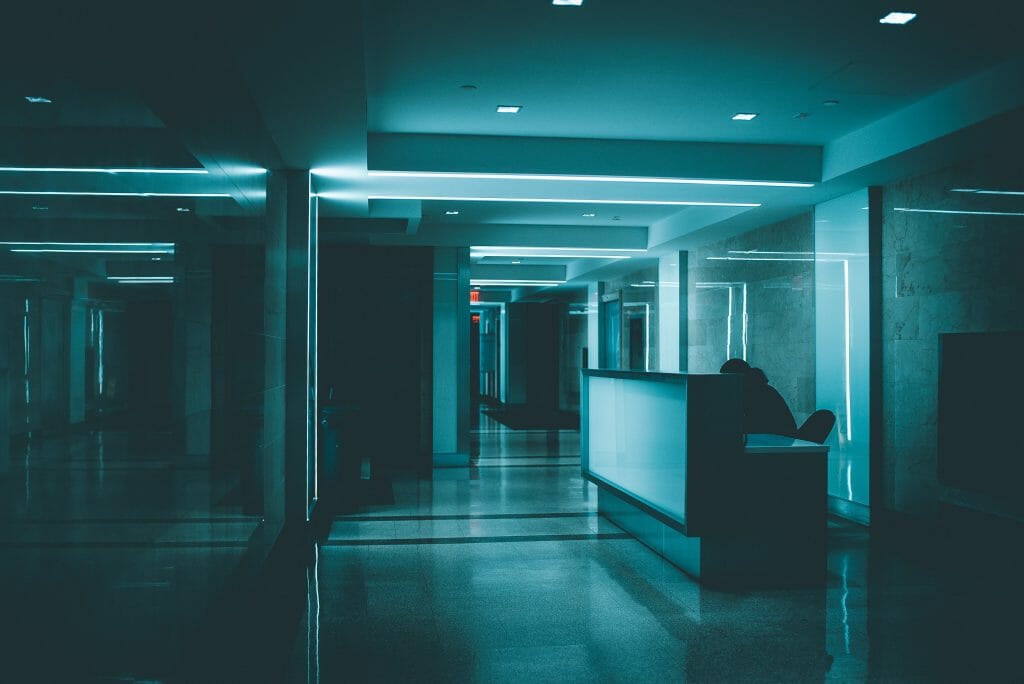 blue light dark hospital hallway with a figure hunched over at the nurse's station